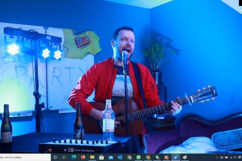 Man met gitaar in kamer met blauw licht tijdens online paasvoorstelling max music.
